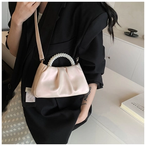Detail of cream pleated cloud bag with pearl handle and slim shoulder strap worn by model