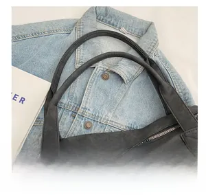Macro view of matte leather tote bag handles with metallic zipper detail on denim jacket