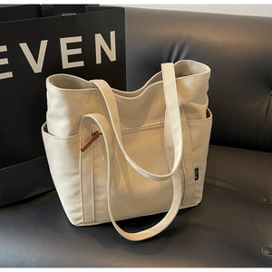 Detailed close-up of a cream canvas tote bag featuring a front zipper pocket and side tags