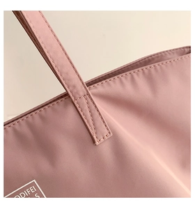 Detail of reinforced stitching on durable grey-pink nylon tote bag with logo