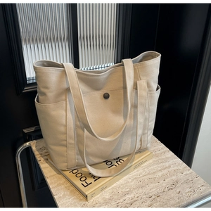 Detailed macro view of oatmeal canvas tote bag featuring a front pocket with black snap button