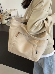 Large beige canvas tote bag with dual handles and side pockets worn by a model