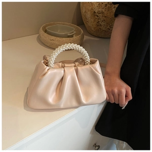 Detail of creamy white cloud bag featuring pleated texture and elegant faux pearl handle