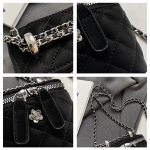 Detail of black quilted mini box bag with silver camellia zipper and chain strap
