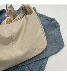 Detail view of beige nylon shoulder bag with Huog logo placed on blue denim fabric