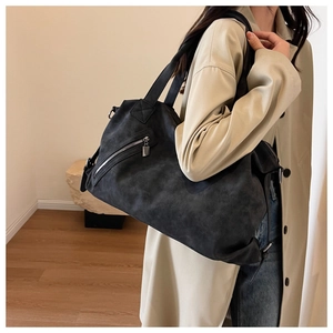 Detail view of black tote bag showing matte texture and slanted zipper pocket with metal lock