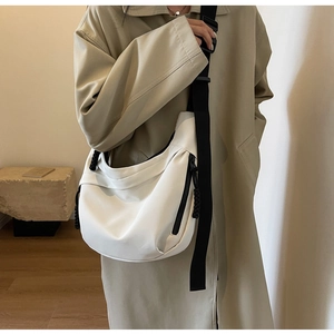 Detailed view of cream nylon crescent crossbody bag worn by model in minimalist studio