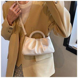 Detail view of cream cloud bag featuring pleated texture and pearl woven handle strap
