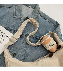 Detail of beige crescent nylon bag with adjustable strap and cute coffee plush charm