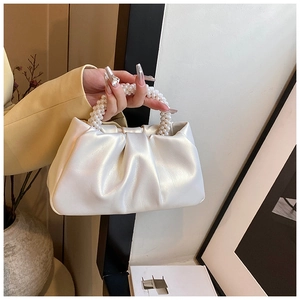 Detail of a pearlescent white cloud bag featuring a pearl bead handle and pleated texture