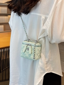 Mint green quilted mini crossbody bag with silver chain and floral charm on a white shirt