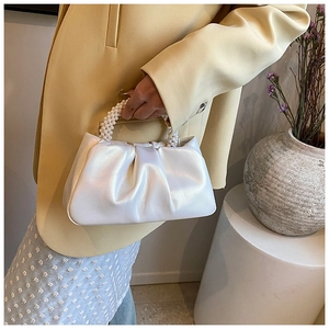 Close-up of elegant white pleated cloud bag with luxury pearl handle held by a model