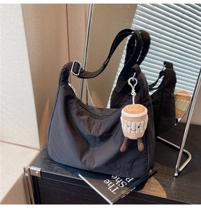 Detail of black nylon shoulder bag with silver buckle and cute coffee cup plush charm
