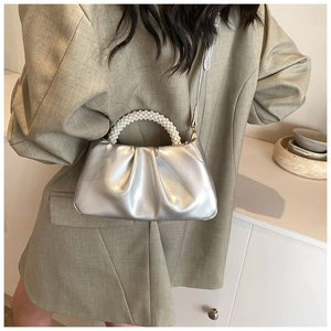 Detail of silver metallic cloud bag featuring large pearl handle and pleated texture