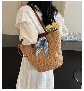 Detail of woven straw tote bag with blue striped scarf and brown leather handle