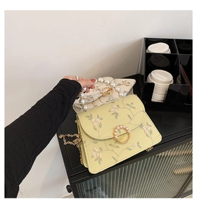 Close-up of elegant floral embroidery and pearl handle detail on a luxury small square bag
