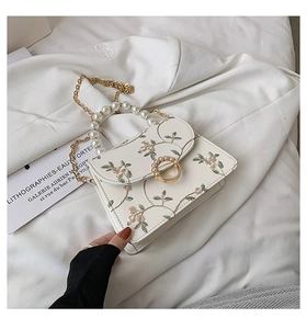 Detail of white lace floral embroidery on handbag with pearl handle and gold chain
