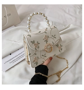 Detail showing elegant white floral embroidery and pearl handle of this stylish handbag