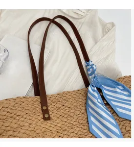 Close-up of woven straw bag with leather handles, metal rivets, and striped silk scarf
