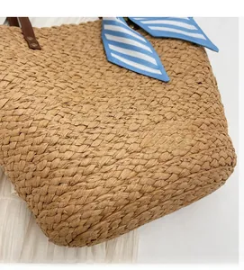 Detail of woven straw tote bag with brown leather straps and striped silk scarf decoration