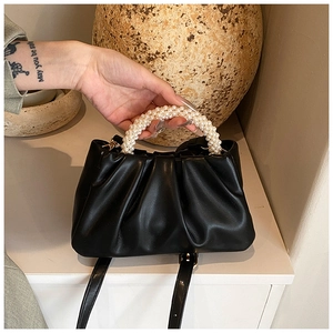 Detail of black pleated cloud bag with elegant pearl beaded handle and slim strap