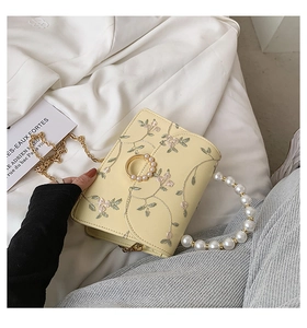 Detailed close-up of floral embroidery on beige bag with pearl chain and metal strap
