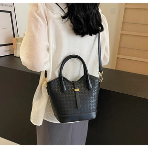 Detail shot of black houndstooth bucket bag with elegant gold hardware on a model