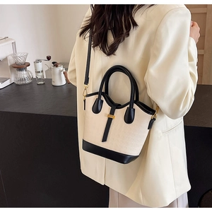 Detail of a beige crocodile pattern bucket bag with black trim and elegant gold buckle