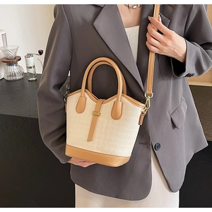 Detail of beige and brown color-block bucket bag with gold hardware and crossbody strap