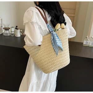 Straw tote bag with brown leather straps and blue striped scarf detail in a cafe setting