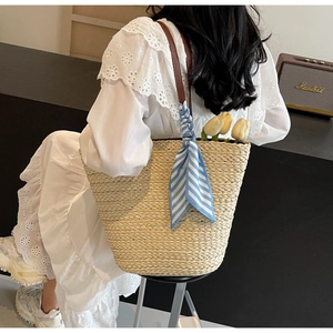 Detail of hand-woven straw tote bag featuring brown leather straps and blue striped scarf