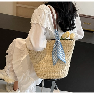Detail view of woven straw tote bag with brown leather straps and blue striped silk scarf