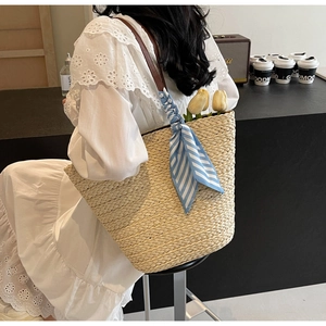 Detail of straw tote bag with brown leather strap and decorative blue striped scarf