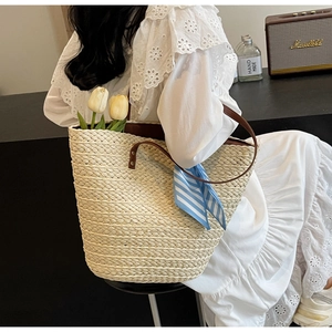 Detail of a beige woven tote bag with brown leather handles and a striped scarf accent