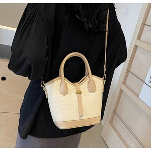 Close-up of cream embossed bucket bag with beige leather trim and gold metal buckle detail
