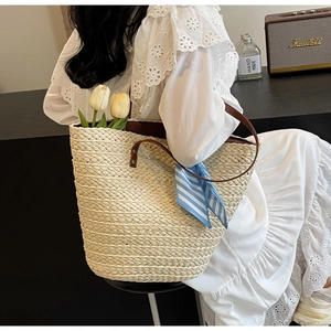Detail of hand-woven straw tote with leather handles and blue striped scarf ornament