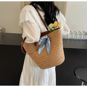 Close-up of woven straw tote bag with blue striped scarf and brown leather shoulder strap