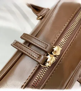Close-up of smooth gold-tone dual zipper closure on a premium brown leather handbag