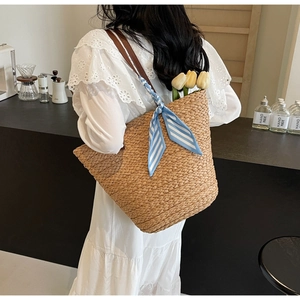 Detail of hand-woven straw tote with leather handles and decorative striped silk scarf