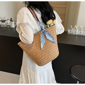 Close-up of woven straw tote bag with leather straps and floral silk scarf detail