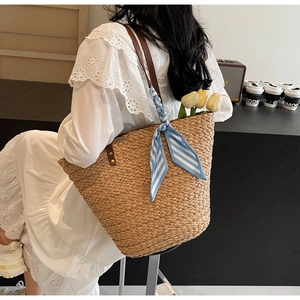 Detail of woven straw tote bag with brown leather strap and blue striped ribbon decor