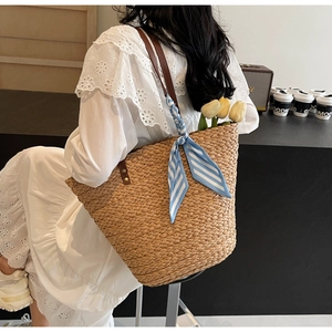 Detail showing handwoven raffia texture with leather handles and striped silk ribbon