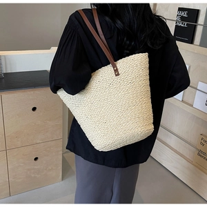 Close-up of woven raffia tote bag with brown leather handles and metallic rivet details