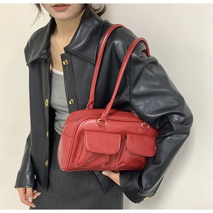 Detail of red glossy leather shoulder bag featuring golden zippers and double front pockets