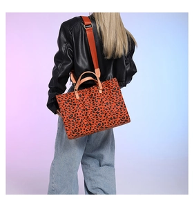Large leopard print tote bag with orange strap shown on model in a stylish setting