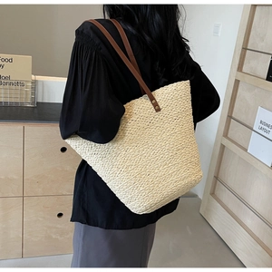 Close-up of beige woven straw tote bag with brown leather handles worn by a model