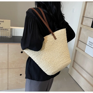 Detail of a cream woven tote bag with brown leather straps in a minimalist home setting