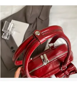 Detail of red glossy PU leather shoulder bag featuring silver metal buckles and dual zippers