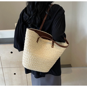 Detail of cream woven straw tote bag with brown leather shoulder straps on a model