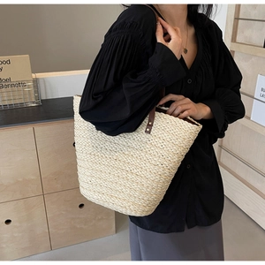 Close-up of beige straw tote bag with brown leather handles and metal rivet details